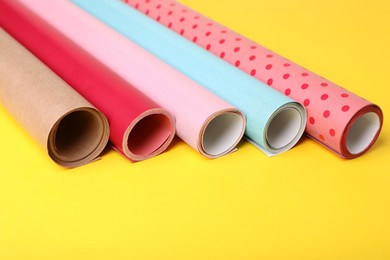 Photo of Rolls of colorful wrapping papers on yellow background, closeup