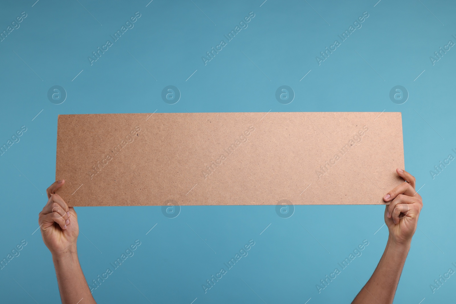 Photo of Man holding blank cardboard banner on light blue background, closeup. Space for text