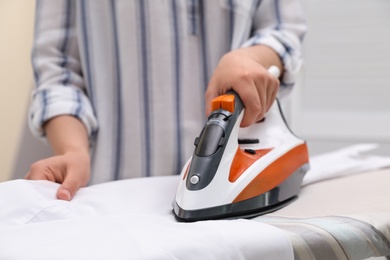 Woman ironing clean shirt on board against color background, closeup with space for text. Laundry day