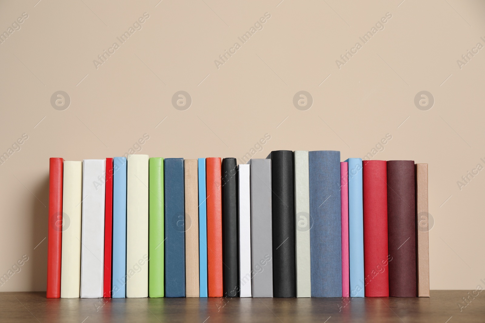 Photo of Many hardcover books on wooden table near beige wall