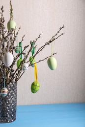 Photo of Beautiful willow branches with painted eggs in vase on light blue table, space for text. Easter decor