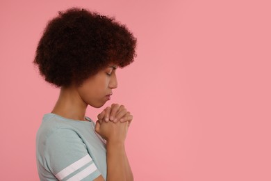 Photo of Woman with clasped hands praying to God on pink background. Space for text