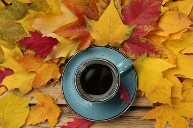 Photo of Cup of hot coffee and autumn leaves on wooden table, flat lay