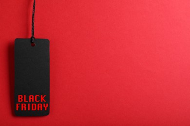 Image of Tag with phrase BLACK FRIDAY on red background, top view. Space for text