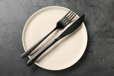 Beige ceramic plate with cutlery on grey table, top view