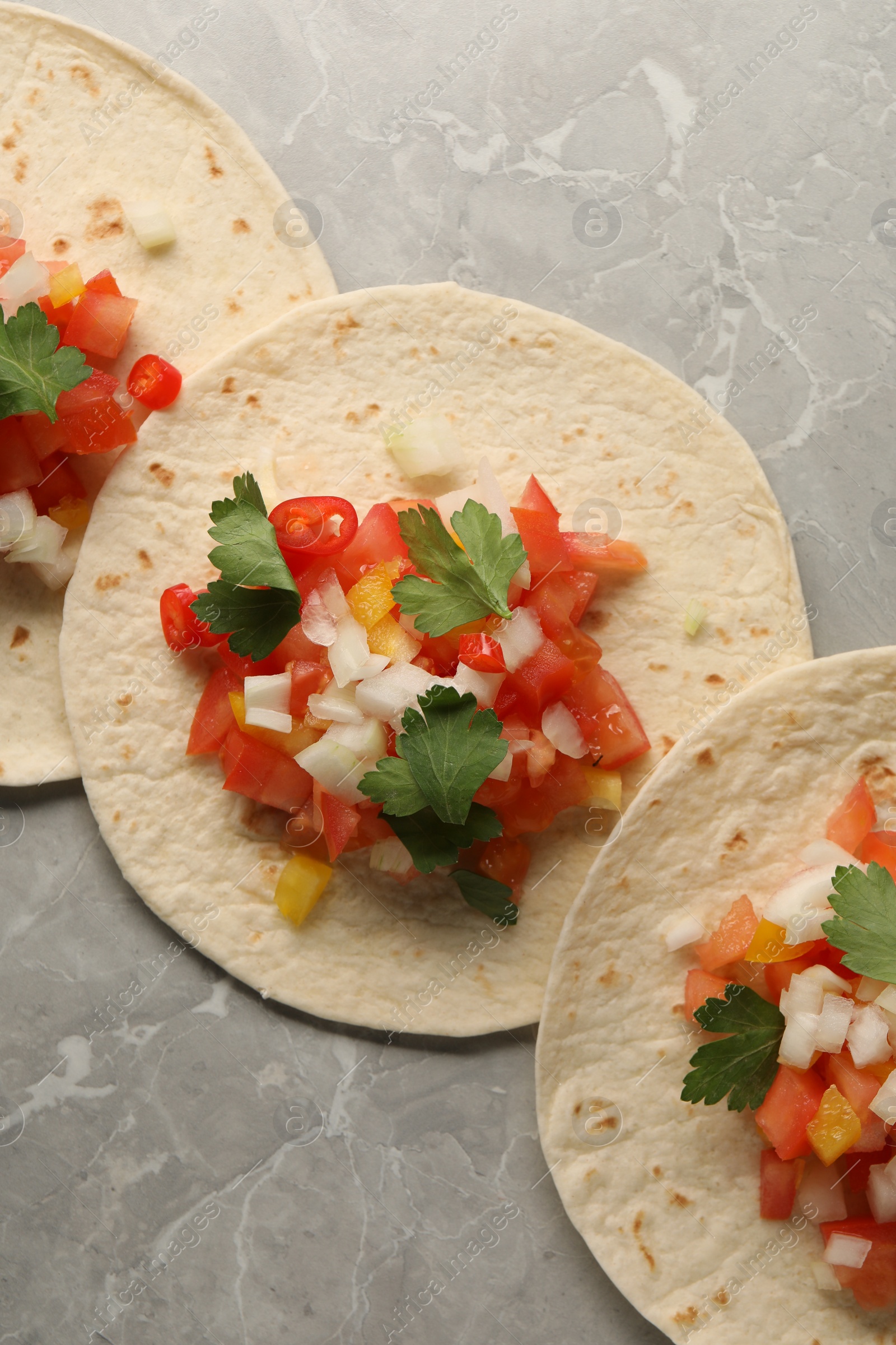 Photo of Delicious tacos with vegetables and parsley on grey marble table, top view