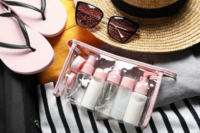 Photo of Plastic bag of cosmetic travel kit and beach accessories in suitcase, top view