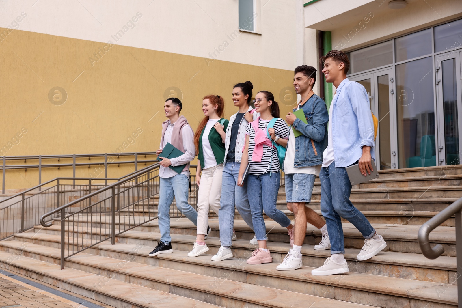 Photo of Group of happy young students walking down stairs outdoors