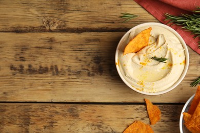 Delicious hummus with nachos and rosemary on wooden table, flat lay. Space for text