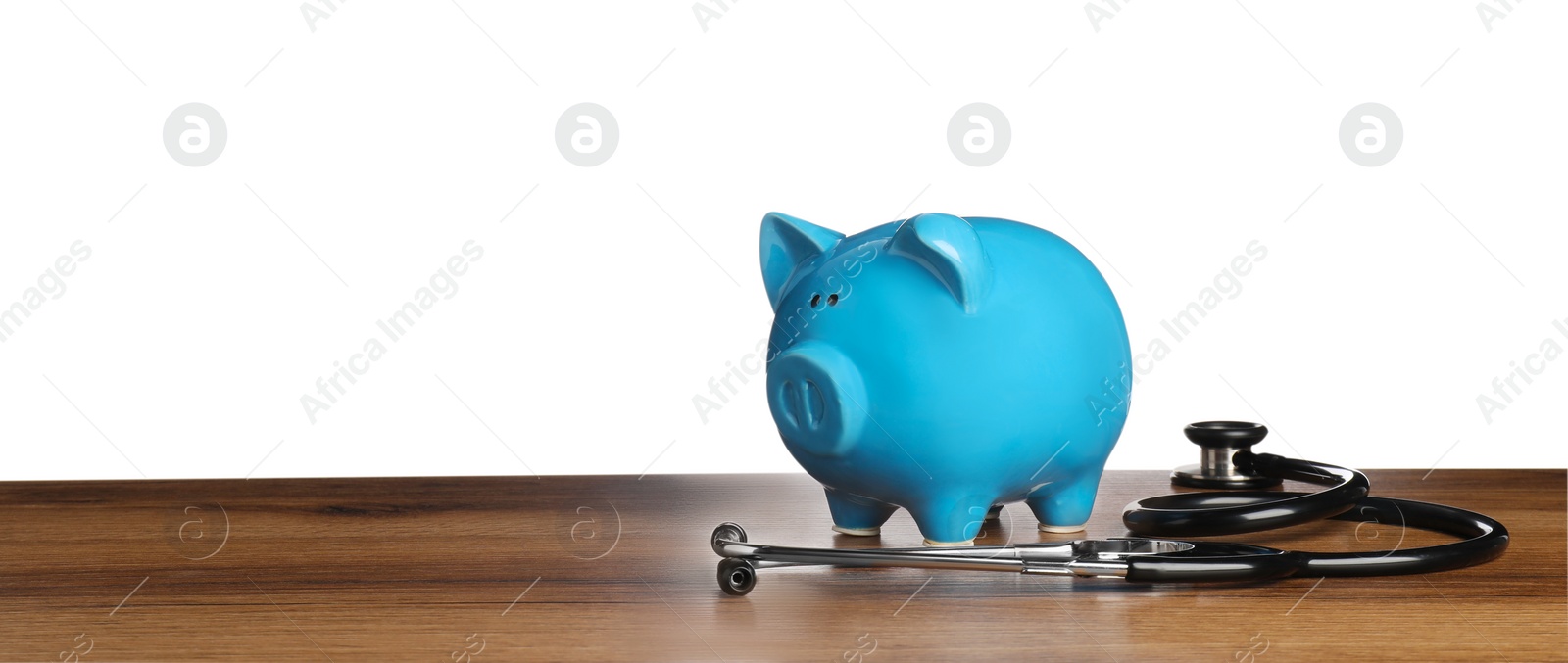 Photo of Piggy bank and stethoscope on wooden table against white background, space for text. Medical insurance