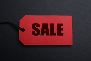 Red tag with word Sale on dark background, top view. Black Friday