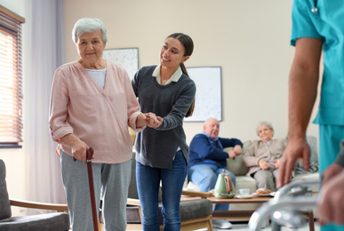 Photo of Care worker helping to elderly woman with stick in geriatric hospice