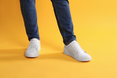 Photo of Man wearing stylish white sneakers on yellow background, closeup