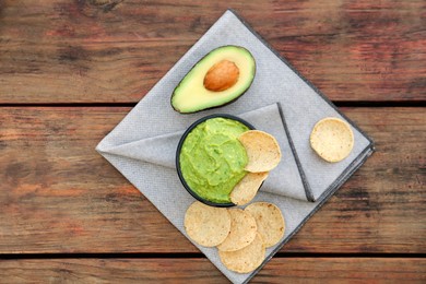 Photo of Delicious guacamole made of avocados with nachos and cut fruit on wooden table, flat lay