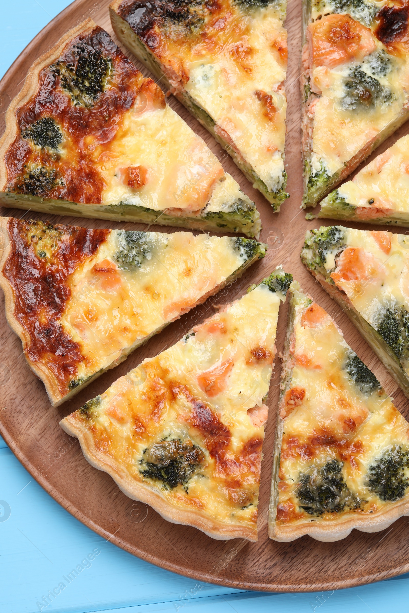 Photo of Delicious homemade quiche with salmon and broccoli on light blue wooden table, top view