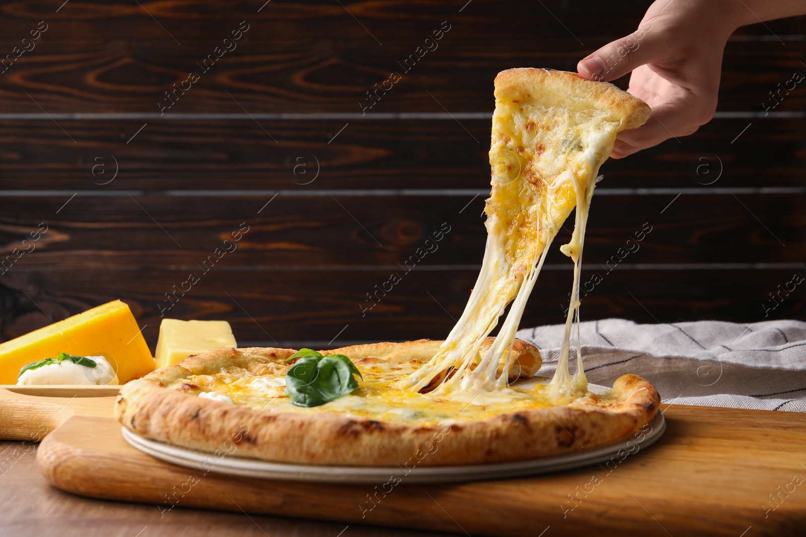 Photo of Woman taking piece of delicious cheese pizza at wooden table, closeup