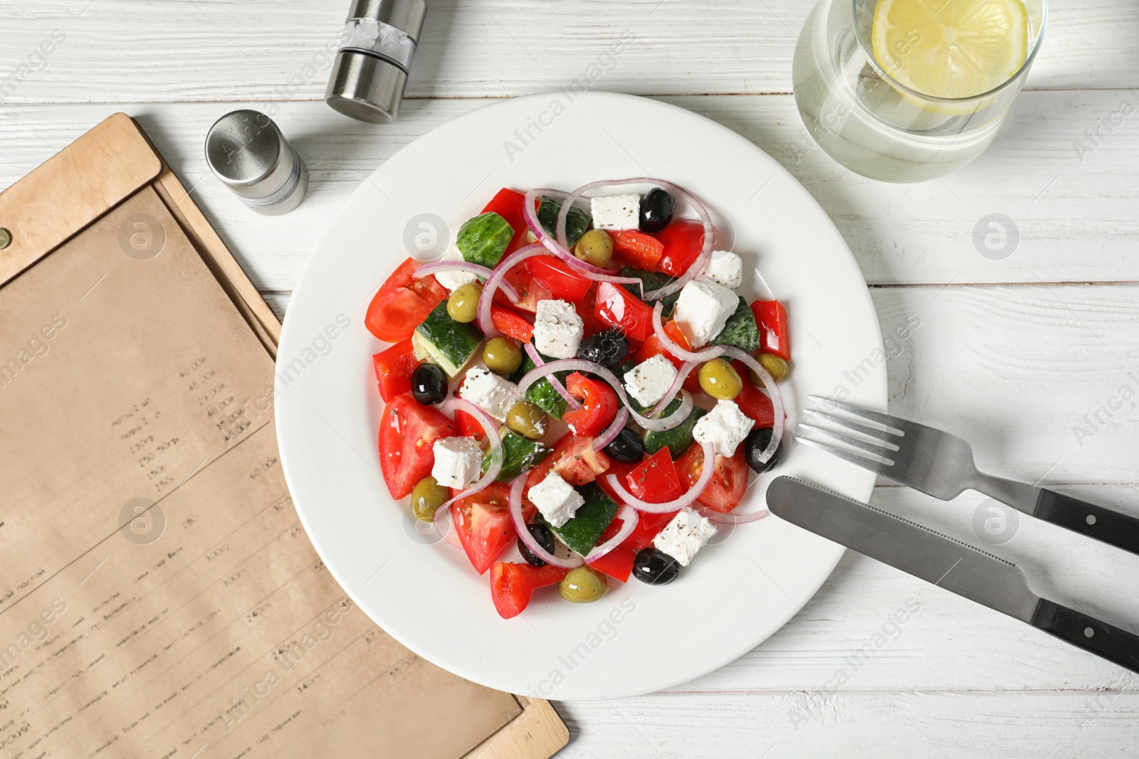 Photo of Plate with delicious Greek salad and menu on table, top view