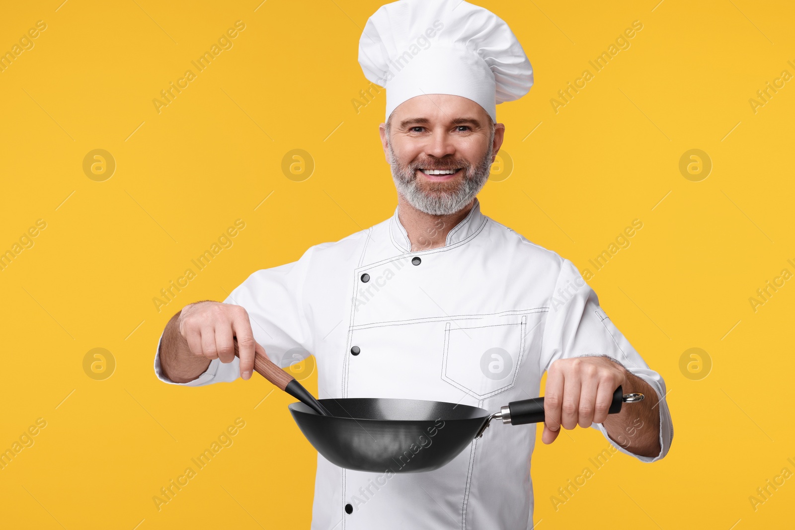 Photo of Happy chef in uniform with wok and spoon on orange background