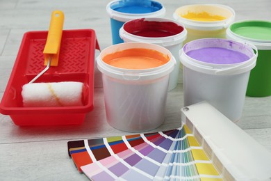 Photo of Buckets of paints, palette and decorator's tools on light wooden background