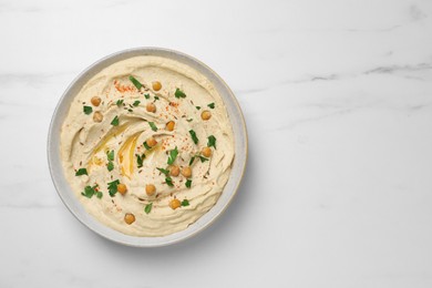 Photo of Tasty hummus with garnish in bowl on white marble table, top view. Space for text