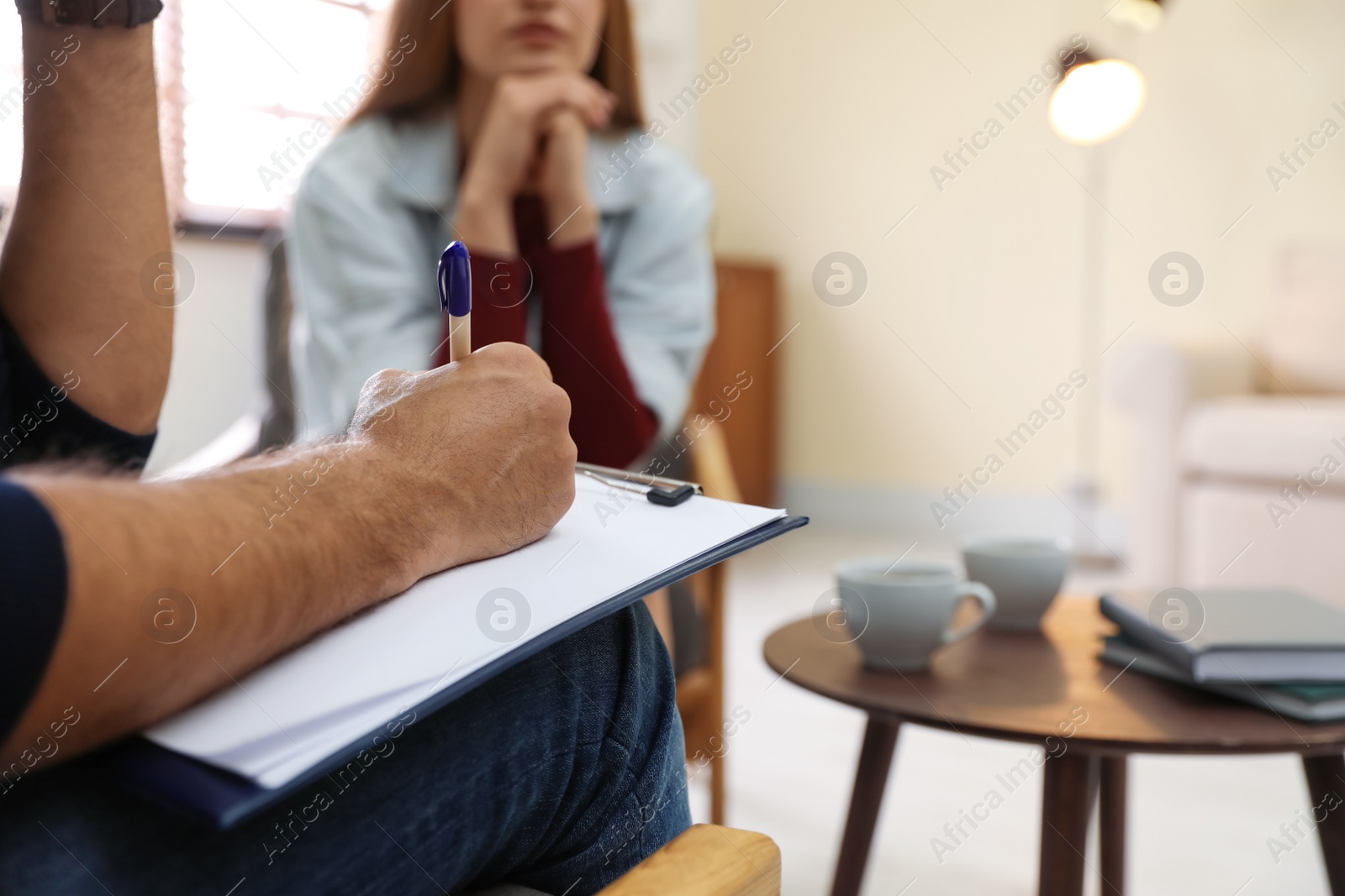 Photo of Professional psychotherapist and patient in office, focus on hands with clipboard