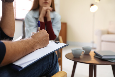 Photo of Professional psychotherapist and patient in office, focus on hands with clipboard