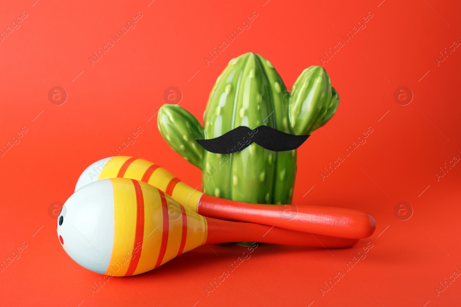 Photo of Colorful maracas, toy cactus with mustache on red background. Musical instrument