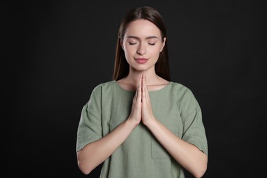 Woman with clasped hands praying on black background