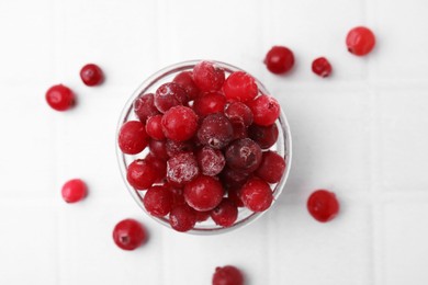 Frozen red cranberries in bowl on white tiled table, flat lay