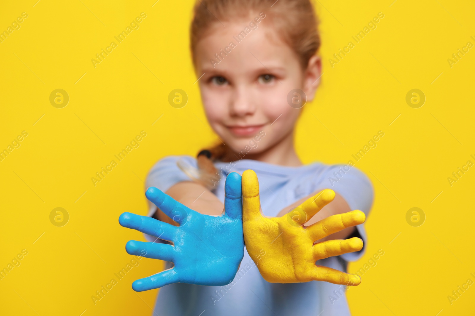 Photo of Little girl with hands painted in Ukrainian flag colors against yellow background, focus on palms. Love Ukraine concept