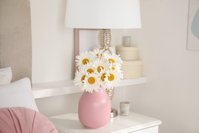 Photo of Bouquet of beautiful daisy flowers and lamp on nightstand in bedroom