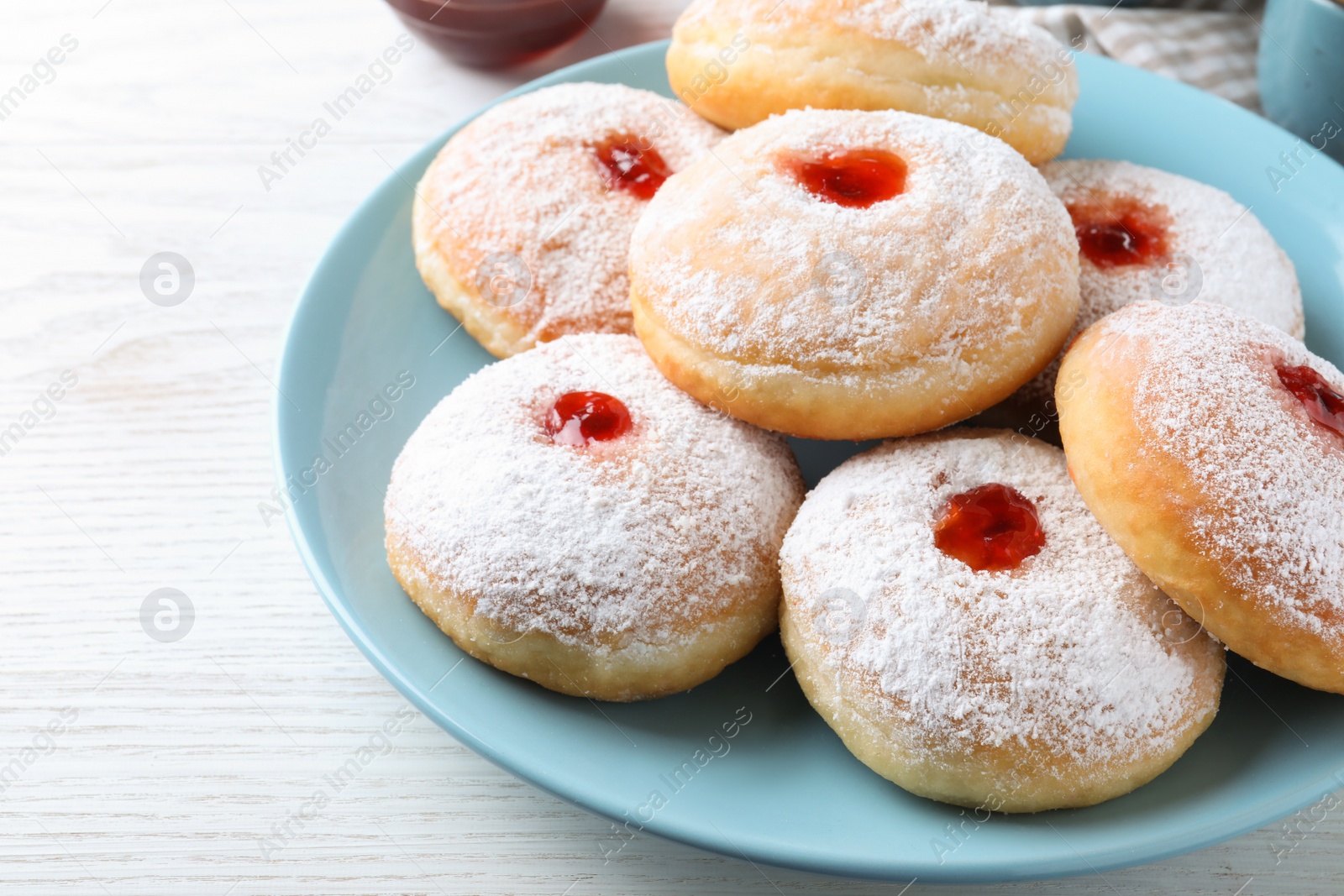 Photo of Delicious donuts with jam and powdered sugar on white table, closeup