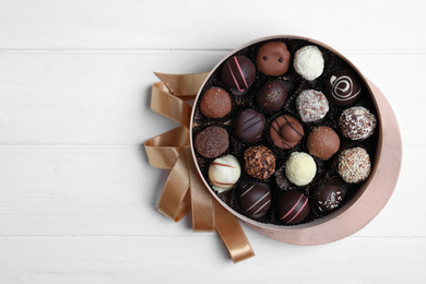 Box with tasty chocolate candies on white wooden table, flat lay