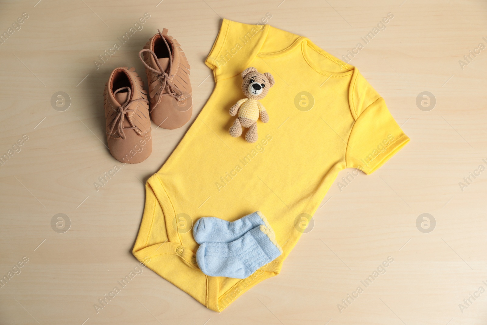 Photo of Baby onesie, shoes, socks and toy bear on wooden table, flat lay