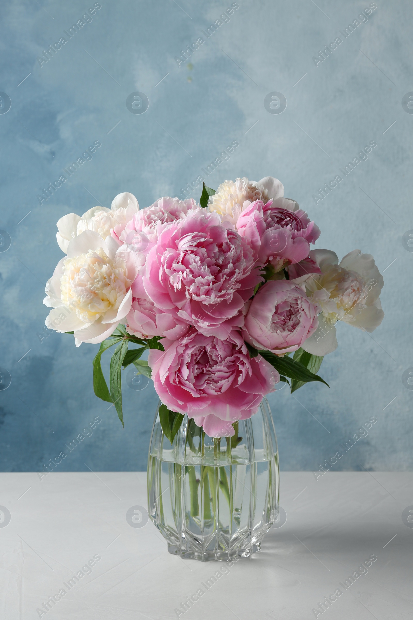 Photo of Bouquet of beautiful peonies in glass vase on white table