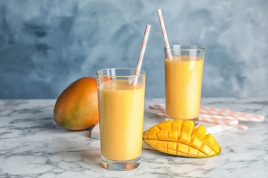 Glasses of fresh mango drink and fruits on table against color background