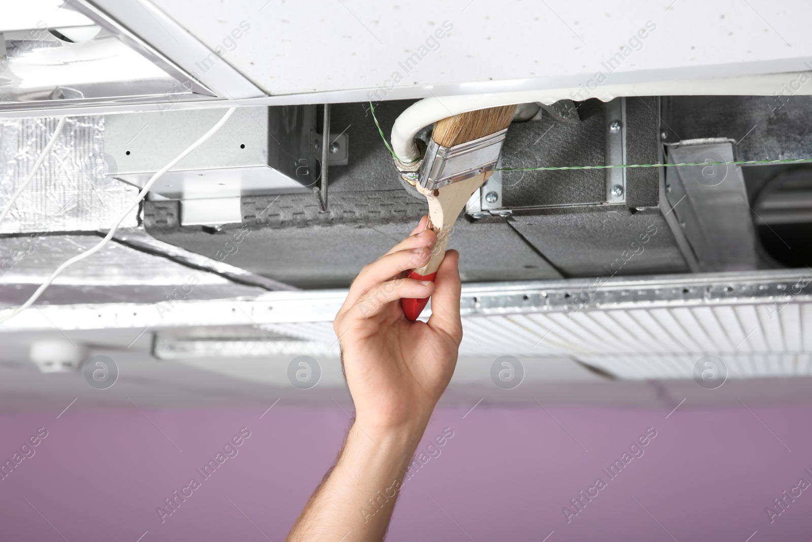 Photo of Young male technician cleaning air conditioner indoors