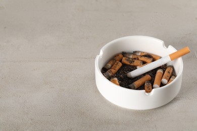 Photo of White ceramic ashtray with cigarette butts on grey table. Space for text