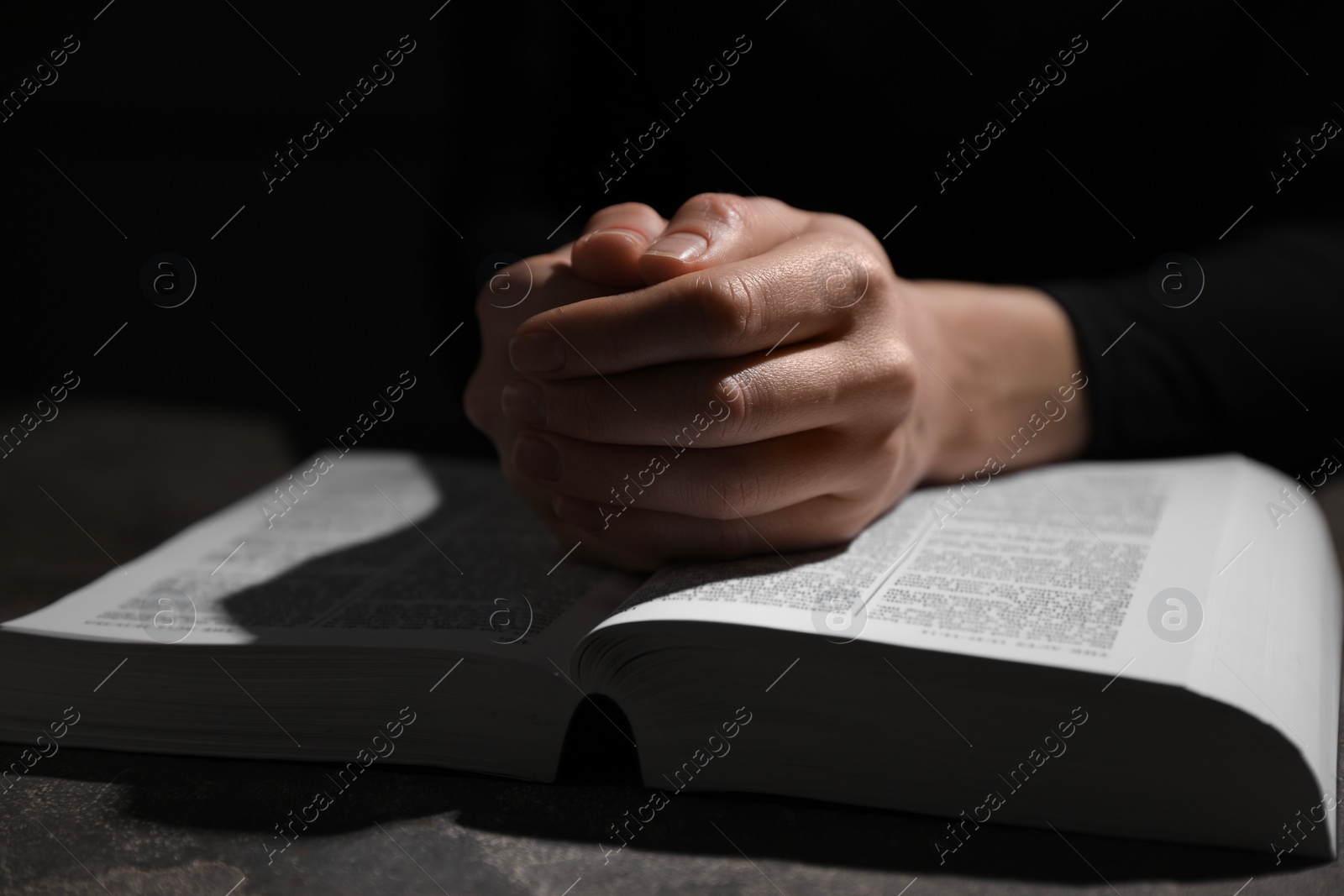 Photo of Religion. Christian woman praying over Bible at table, closeup