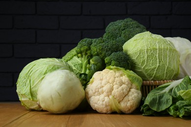 Photo of Many different types of fresh cabbage on wooden table near brick wall