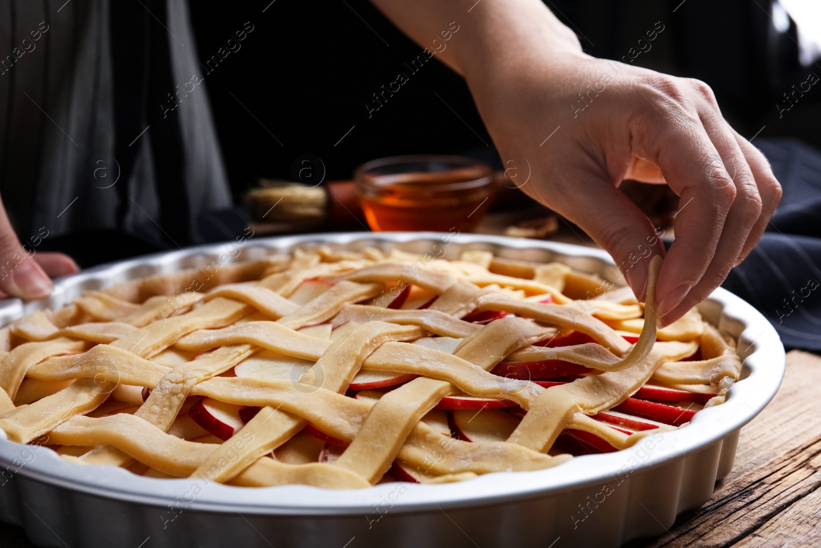 Photo of Woman making lattice top for traditional English apple pie at wooden table, closeup