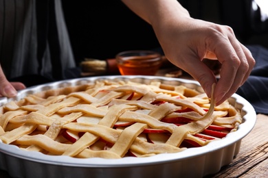 Woman making lattice top for traditional English apple pie at wooden table, closeup