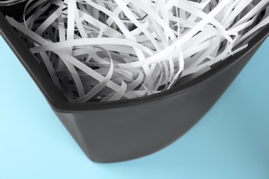 Photo of Shredded paper strips in trash bin on light blue background, closeup