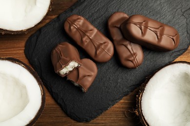 Photo of Delicious milk chocolate candy bars with coconut filling on wooden table, flat lay