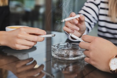Photo of Women holding cigarette over glass ashtray at table, closeup