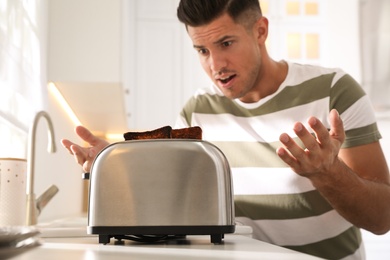 Emotional man near toaster with slices of burnt bread in kitchen