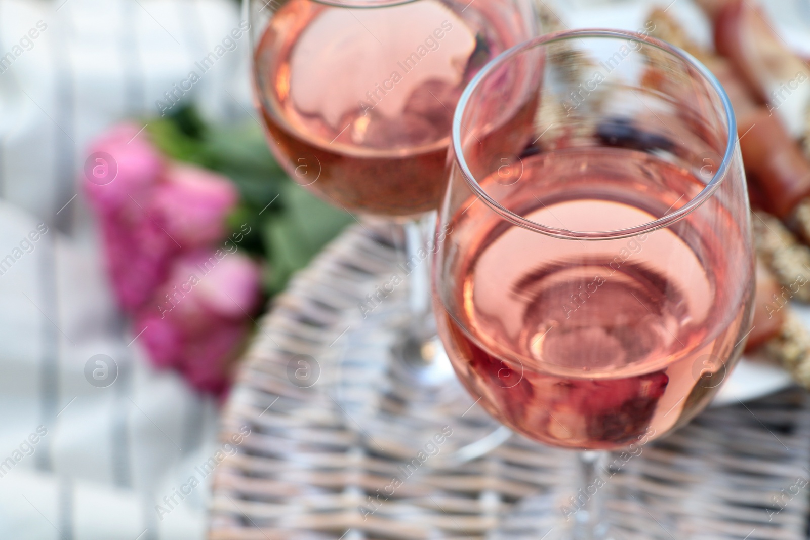 Photo of Glasses of delicious rose wine and food on picnic basket outdoors