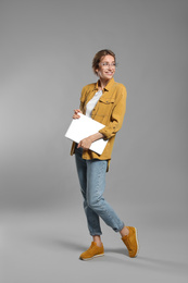 Full length portrait of young woman with modern laptop on grey background