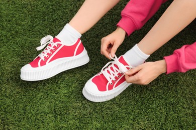Woman tying shoelace of classic old school sneaker on green grass outdoors, above view