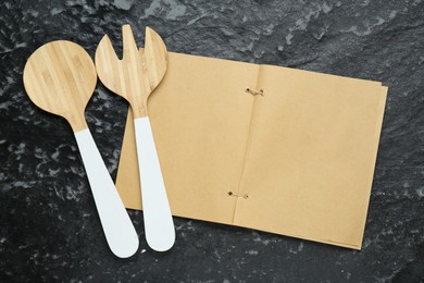 Photo of Blank recipe book and wooden utensils on black textured table, flat lay. Space for text